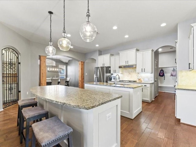 17806 Creek Bluff Ln, Cypress, TX 77433 - kitchen with arched walkways, a center island with sink, appliances with stainless steel finishes, white cabinets, and recessed lighting