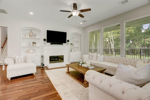 3350 Precinct Line Rd, Richmond, TX 77406 - living room with built in shelves, wood finished floors, a ceiling fan, a glass covered fireplace, and stairs
