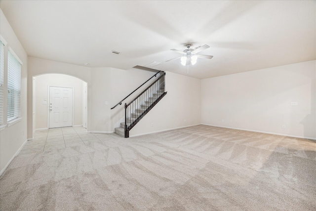 18621 Serenity Loch Dr, Spring, TX 77379 - unfurnished living room with light colored carpet, stairs, arched walkways, ceiling fan, and baseboards