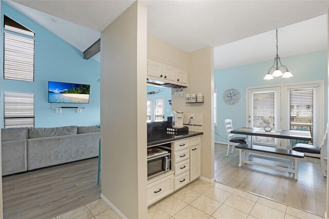 1114 Tiki Dr, Galveston, TX 77554 - kitchen featuring stainless steel microwave, white cabinets, light wood-style flooring, dark countertops, and hanging light fixtures