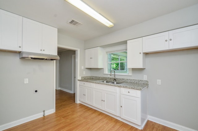 4514 Keystone St, Houston, TX 77021 - kitchen with a sink, under cabinet range hood, light wood-style flooring, baseboards, and white cabinetry