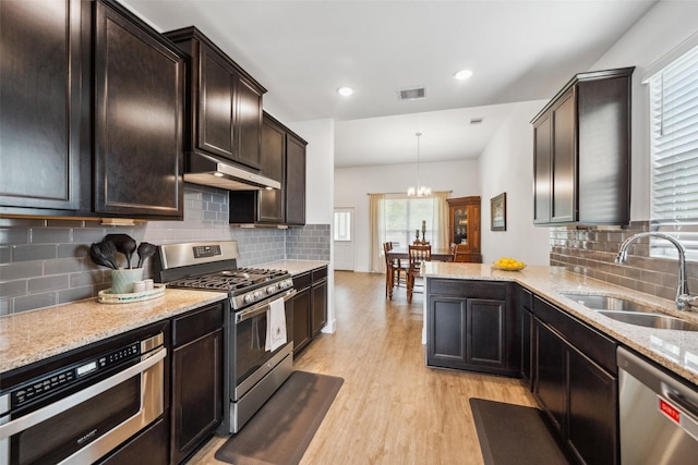 6006 Hazel Place Dr, Conroe, TX 77303 - kitchen featuring stainless steel appliances, a sink, under cabinet range hood, light wood finished floors, and a chandelier