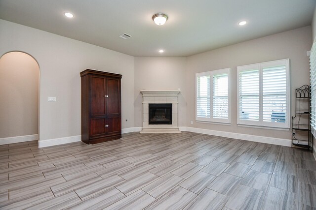 2334 Twin Rose Dr, Missouri City, TX 77459 - unfurnished living room featuring a glass covered fireplace, baseboards, light wood finished floors, arched walkways, and recessed lighting