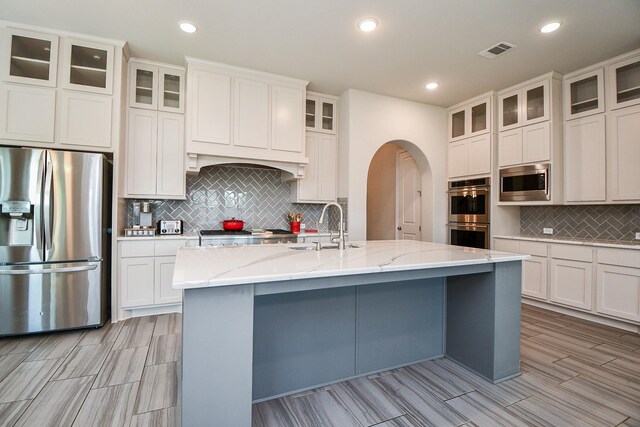 2334 Twin Rose Dr, Missouri City, TX 77459 - kitchen featuring appliances with stainless steel finishes, a sink, backsplash, a center island with sink, and light stone countertops