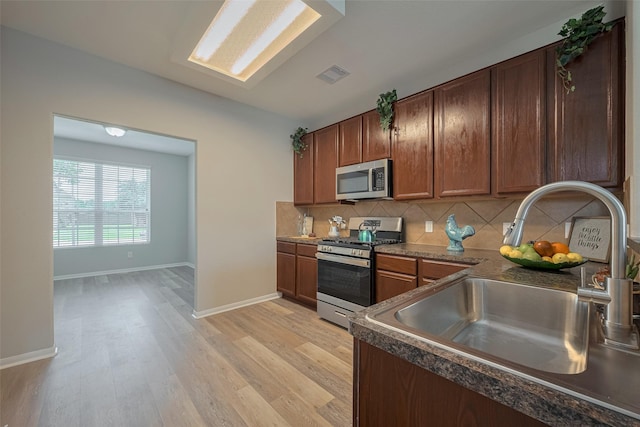 2810 Meadowbrook Ln, Rosenberg, TX 77471 - kitchen with stainless steel appliances, a sink, dark countertops, and light wood finished floors