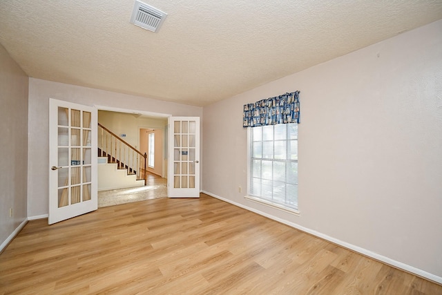 19515 Oak Timbers Dr, Humble, TX 77346 - empty room featuring french doors, light wood finished floors, baseboards, stairs, and a textured ceiling