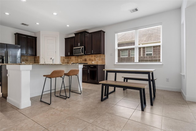 2206 Hidden Meadow Ln, Pearland, TX 77089 - kitchen with stainless steel microwave, decorative backsplash, a kitchen bar, recessed lighting, and refrigerator with ice dispenser