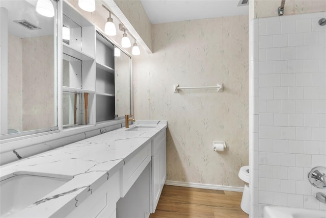 8903 Roos Rd, Houston, TX 77036 - bathroom featuring wood finished floors, double vanity, toilet, wallpapered walls, and baseboards