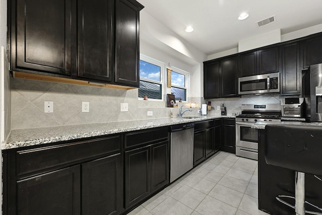 2507 Ocean Pass Ln, Richmond, TX 77469 - kitchen featuring stainless steel appliances, dark cabinetry, light stone counters, light tile patterned flooring, and recessed lighting