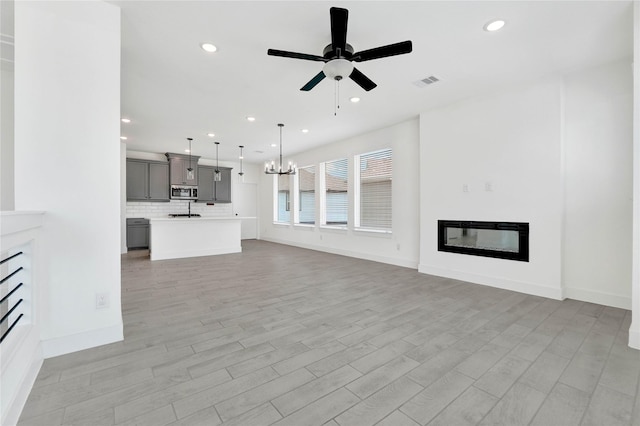 15147 Colorado Bend Park Dr, Cypress, TX 77433 - unfurnished living room featuring a glass covered fireplace, ceiling fan, a chandelier, recessed lighting, and light wood-type flooring