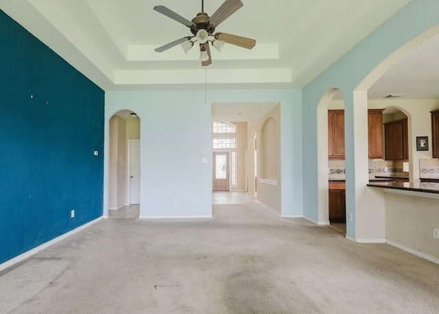 4615 Long Climb Cyn, Humble, TX 77396 - unfurnished living room with a ceiling fan, a tray ceiling, light carpet, and arched walkways
