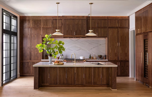 2218 Bartlett St, Houston, TX 77098 - kitchen featuring light countertops, light wood-type flooring, an island with sink, pendant lighting, and crown molding