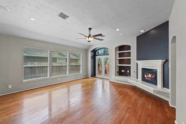 7931 Clarion Way, Houston, TX 77040 - unfurnished living room featuring built in shelves, wood finished floors, a textured ceiling, ceiling fan, and a glass covered fireplace