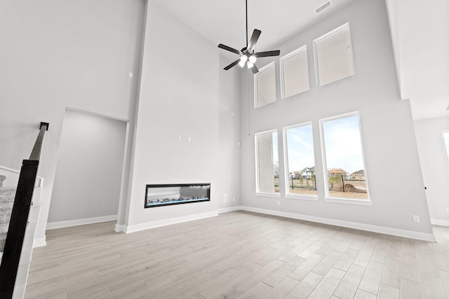 5049 Steady Breeze Dr, Katy, TX 77493 - unfurnished living room featuring a towering ceiling, a glass covered fireplace, light wood-style flooring, baseboards, and ceiling fan