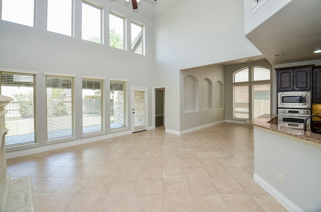 9819 St Romain Dr, Katy, TX 77494 - unfurnished living room with light tile patterned floors, ceiling fan, a high ceiling, plenty of natural light, and baseboards