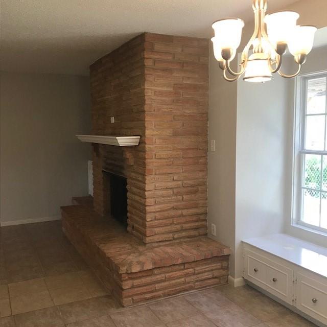 5471 Kuldell Dr, Houston, TX 77096 - unfurnished living room featuring a chandelier, light tile patterned floors, baseboards, and a brick fireplace