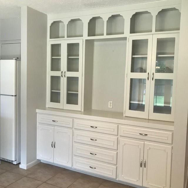 5471 Kuldell Dr, Houston, TX 77096 - kitchen with freestanding refrigerator, dark tile patterned floors, glass insert cabinets, and light countertops