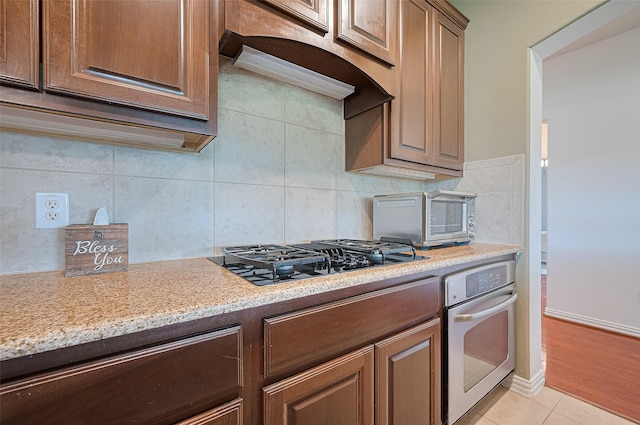 17207 Red Oak Bend Dr, Cypress, TX 77433 - kitchen featuring oven, black gas cooktop, backsplash, light tile patterned flooring, and light stone countertops