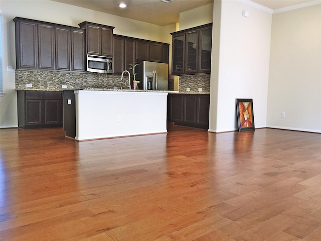 3004 Fairdale Estates Ct, Houston, TX 77057 - kitchen featuring appliances with stainless steel finishes, crown molding, tasteful backsplash, a center island with sink, and light wood-style floors
