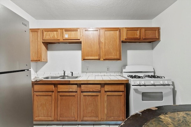 2905 Glenwood St, Beaumont, TX 77705 - kitchen featuring freestanding refrigerator, white gas stove, a sink, tile counters, and brown cabinetry