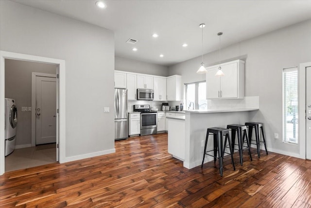 15202 Cavalier Canyon Dr, Lakeway, TX 78734 - kitchen with appliances with stainless steel finishes, dark wood-type flooring, a peninsula, washer / dryer, and a breakfast bar area