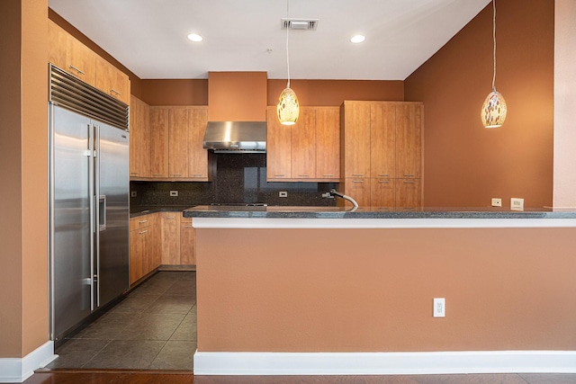 4821 Nasa Pkwy Unit 12E, Pasadena, TX 77586 - kitchen featuring built in refrigerator, wall chimney range hood, decorative backsplash, dark countertops, and pendant lighting