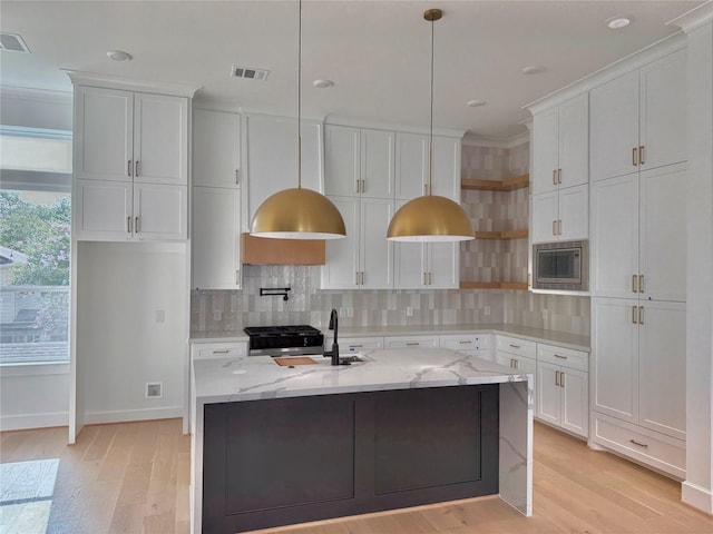 923 Fisher St Unit B, Houston, TX 77018 - kitchen with stainless steel microwave, light wood-style floors, white cabinetry, decorative backsplash, and a center island with sink