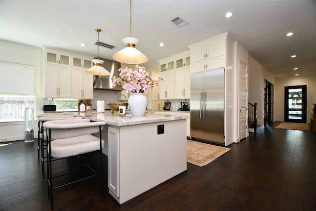 802 W 30th St, Houston, TX 77018 - kitchen with stainless steel built in refrigerator, wall chimney range hood, recessed lighting, dark wood-style flooring, and an island with sink