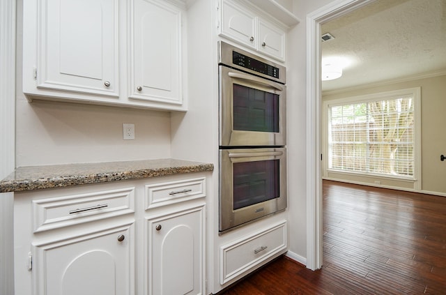 1927 Willowlake Dr, Houston, TX 77077 - kitchen with stainless steel double oven, baseboards, dark wood-type flooring, light stone countertops, and white cabinetry