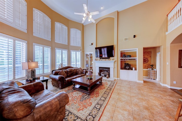 4815 N Pine Brook Way, Houston, TX 77059 - living room featuring built in shelves, a high ceiling, a glass covered fireplace, ceiling fan, and light tile patterned flooring