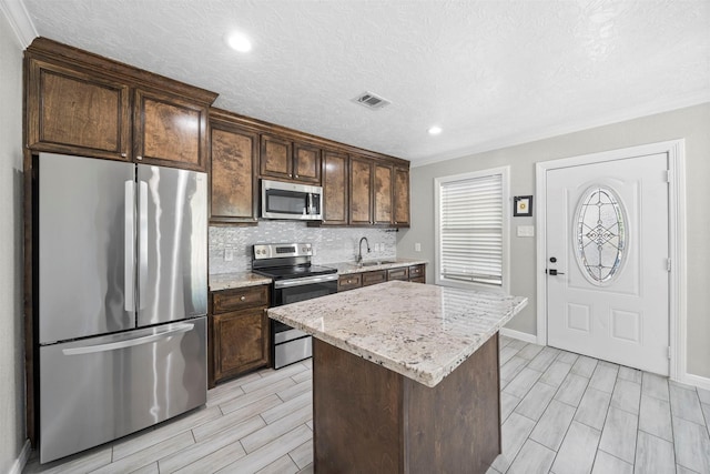 7941 Goode St, Houston, TX 77012 - kitchen with appliances with stainless steel finishes, wood tiled floors, tasteful backsplash, a kitchen island, and dark brown cabinetry
