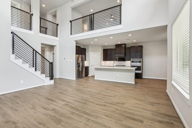 29211 Pikes Peak Dr, Katy, TX 77494 - unfurnished living room with a towering ceiling, light wood-type flooring, baseboards, stairs, and a sink