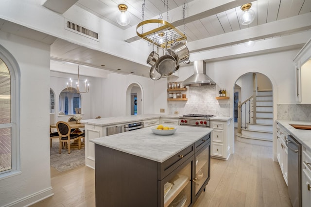11 Twin Circle Dr, Houston, TX 77042 - kitchen featuring arched walkways, wall chimney exhaust hood, light wood-style flooring, stainless steel dishwasher, and white cabinetry