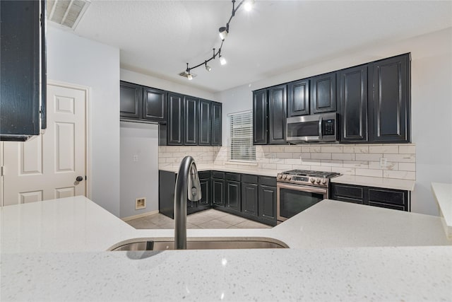 19315 Oak Station Dr, Humble, TX 77346 - kitchen featuring stainless steel appliances, a sink, light stone counters, dark cabinetry, and tasteful backsplash