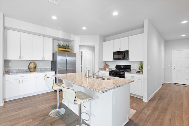 10530 Vinca Minor Ln, Houston, TX 77016 - kitchen featuring black appliances, a sink, a breakfast bar area, recessed lighting, and an island with sink