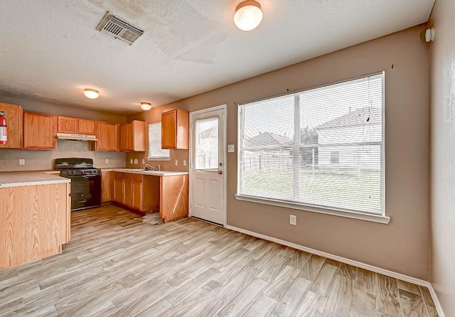 1406 Hade Falls Ln, Houston, TX 77073 - kitchen featuring black range with gas stovetop, under cabinet range hood, light countertops, light wood-style floors, and baseboards
