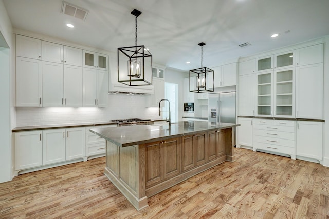 1243 Candlelight Ln, Houston, TX 77018 - kitchen featuring stainless steel built in refrigerator, light wood-type flooring, tasteful backsplash, dark countertops, and a center island with sink