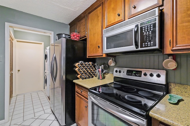 2893 Panagard Dr Unit 42, Houston, TX 77082 - kitchen with stainless steel appliances, stacked washer and clothes dryer, light tile patterned floors, brown cabinetry, and light stone countertops