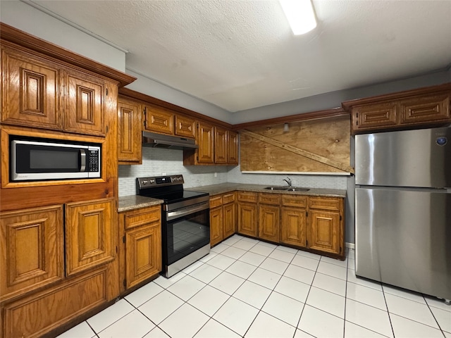 10509 Kelburn Dr, Houston, TX 77016 - kitchen with stainless steel appliances, under cabinet range hood, a sink, brown cabinetry, and tasteful backsplash