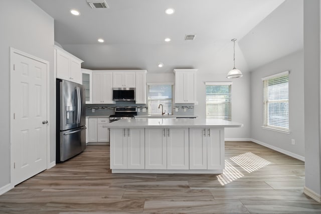 146 S Star Ridge Cir, The Woodlands, TX 77382 - kitchen featuring appliances with stainless steel finishes, lofted ceiling, light countertops, white cabinets, and a center island