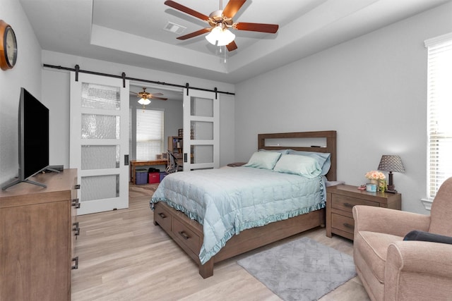 5746 Lakeside Villas Ct, Conroe, TX 77304 - bedroom featuring a barn door, a raised ceiling, light wood-style floors, and ceiling fan