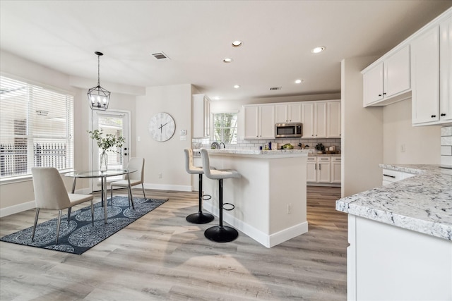 13411 SE Via Chianti Ln, Cypress, TX 77429 - kitchen with stainless steel microwave, backsplash, white cabinets, light wood-type flooring, and recessed lighting