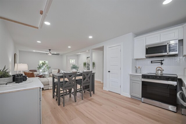 7406 Valeda Dr, Deer Park, TX 77536 - kitchen featuring stainless steel microwave, black electric range oven, light wood-style floors, decorative backsplash, and light countertops