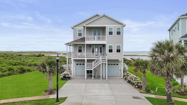 3903 Evening Primrose Dr, Galveston, TX 77554 - coastal inspired home with a balcony, driveway, a front lawn, a water view, and an attached garage
