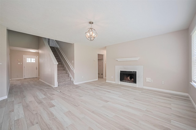 16502 N Glade Dr, Houston, TX 77073 - unfurnished living room with stairs, light wood finished floors, a chandelier, baseboards, and a tile fireplace