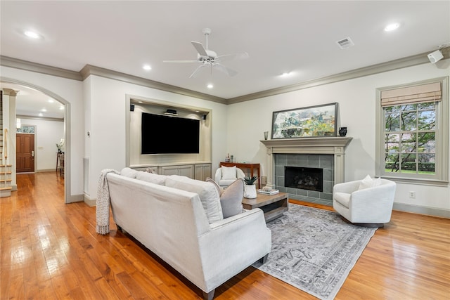 3502 Underwood St, Houston, TX 77025 - living room featuring ornamental molding, a ceiling fan, light wood-style flooring, a tile fireplace, and arched walkways