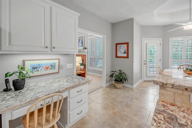 3008 Cochise Ct, College Station, TX 77845 - kitchen featuring white cabinets, baseboards, light stone counters, light tile patterned flooring, and ceiling fan