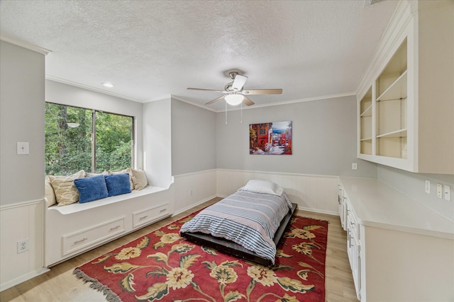 2411 Oakbank Dr, Houston, TX 77339 - bedroom featuring light wood finished floors, a textured ceiling, wainscoting, crown molding, and a ceiling fan