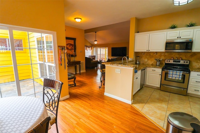 13555 Portobello Dr, Houston, TX 77083 - kitchen with stainless steel appliances, open floor plan, a peninsula, light wood-style flooring, and white cabinetry