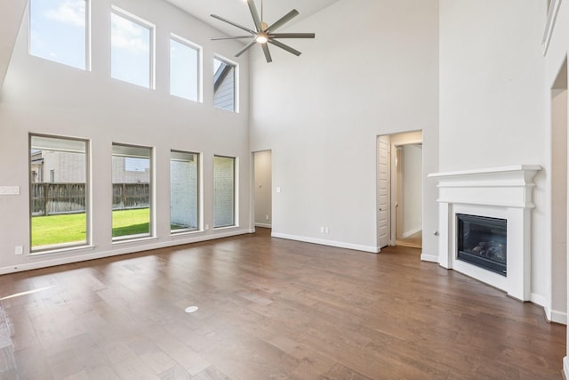28814 Creekside Bend Dr, Fulshear, TX 77441 - unfurnished living room featuring ceiling fan, a high ceiling, a glass covered fireplace, dark wood-style flooring, and baseboards